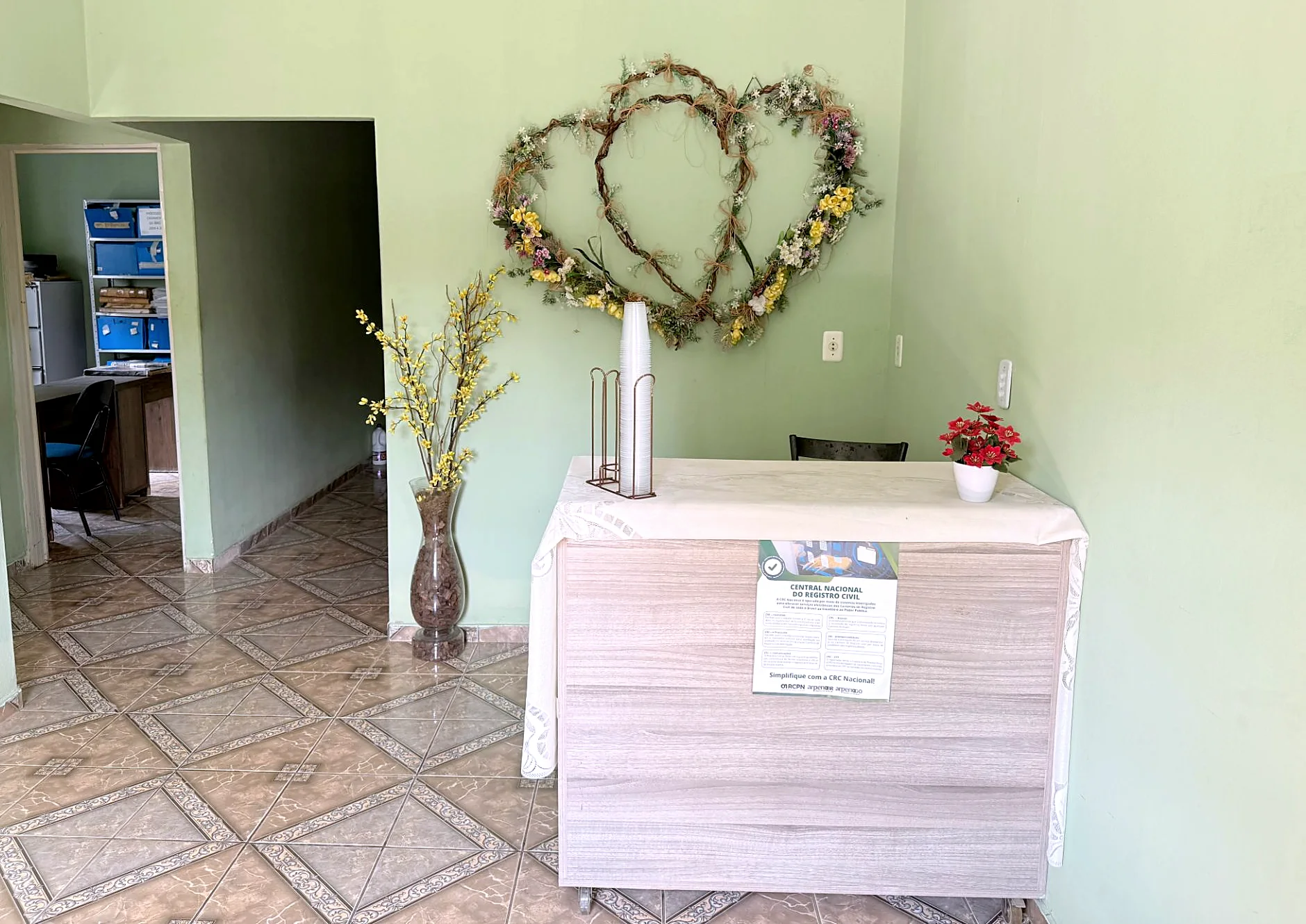 Recepção do cartório, com o balcão de atendimento e um arranjo de flores em forma de dois corações na parede